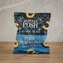 Load image into Gallery viewer, A bag of Awfully Posh Pork Crackling, Simply Salted, standing upright on a wooden surface against a textured gray background.
