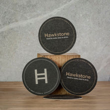 Load image into Gallery viewer, Three round dark coaster-like drink coasters with the brand name Hawkstone printed on them.
